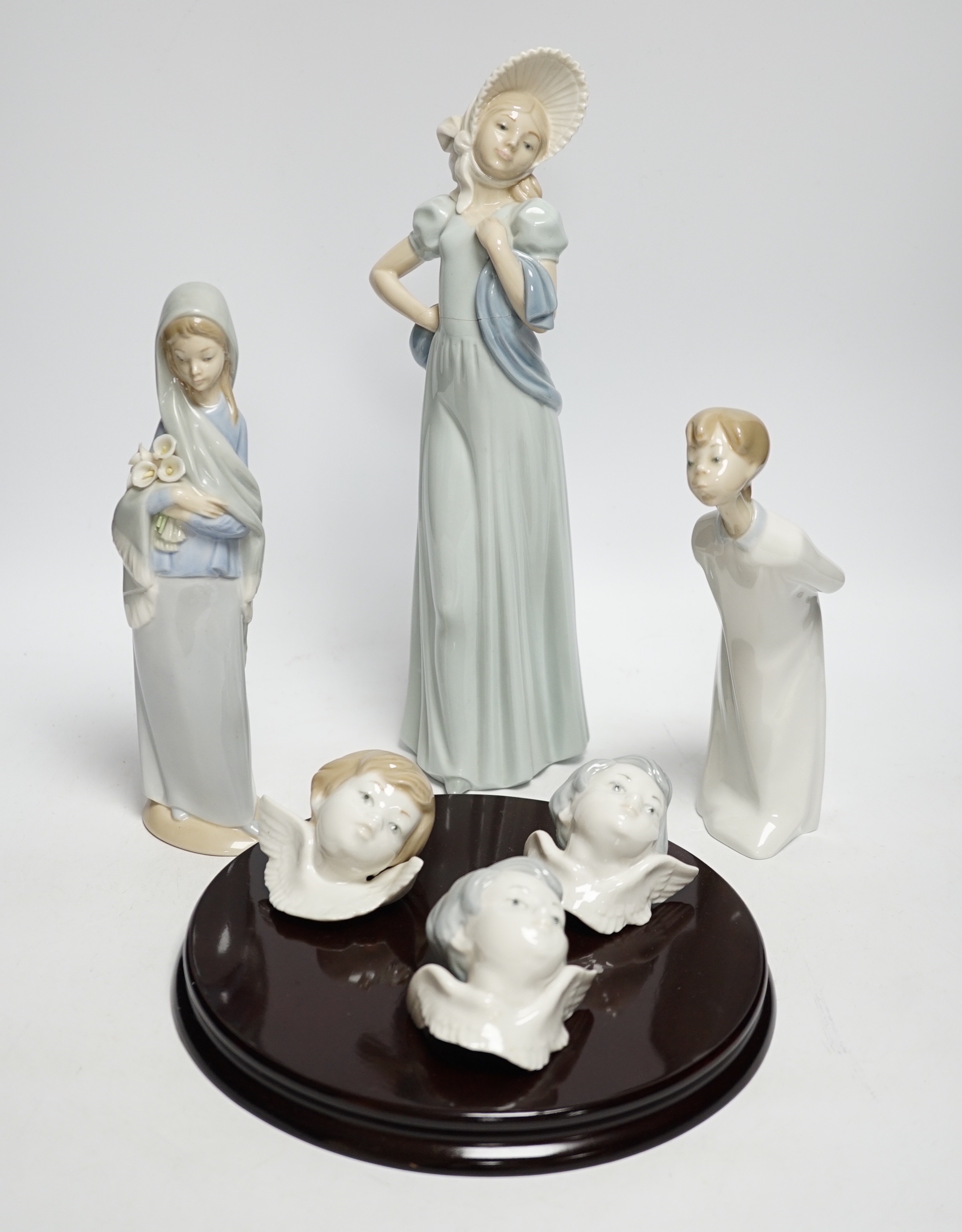 A Lladro circular wooden plaque with three angelic faces, four models of children, an angel, female figure in a hat another and glazed plaque (9) tallest 32cm high